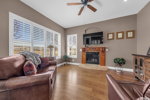 living area with wood finished floors, a tiled fireplace, a ceiling fan, and baseboards