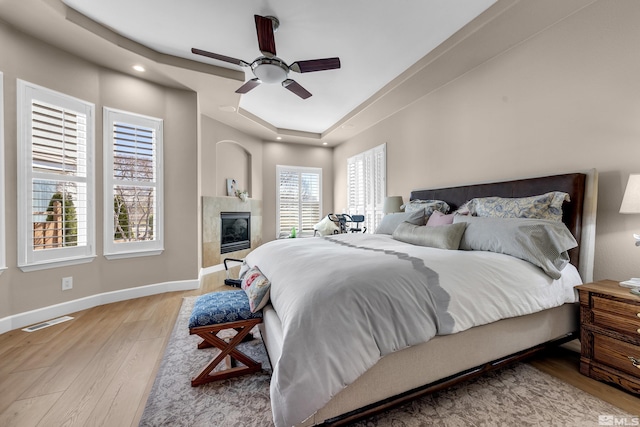 bedroom with ceiling fan, light wood-type flooring, visible vents, a tiled fireplace, and baseboards