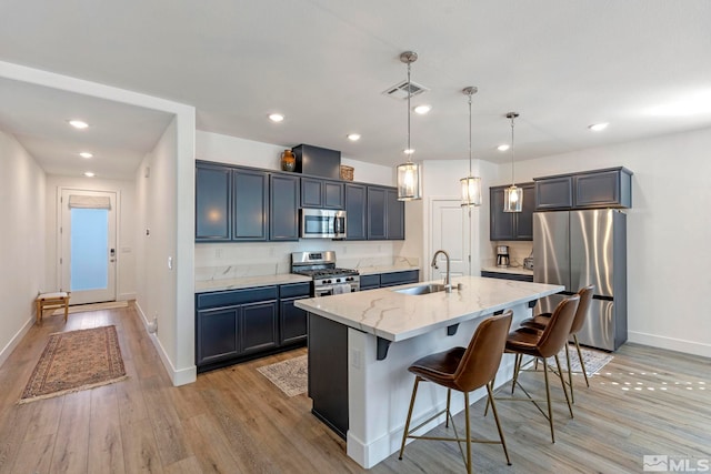 kitchen with a kitchen bar, visible vents, appliances with stainless steel finishes, light stone counters, and a sink