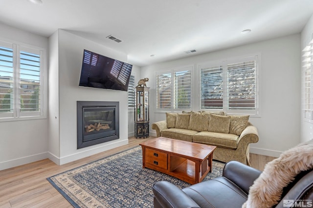 living room featuring light wood-style floors, baseboards, a glass covered fireplace, and visible vents