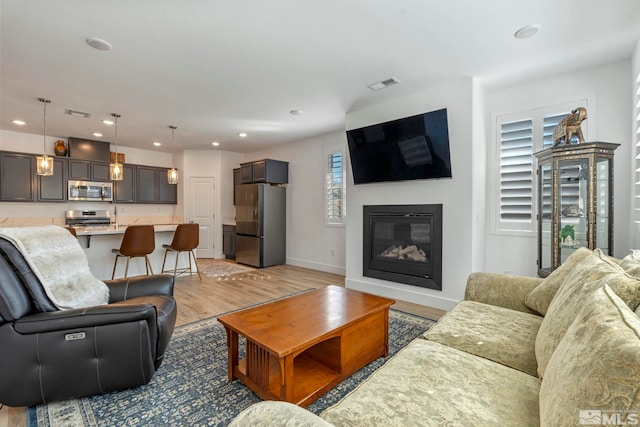 living area with visible vents, baseboards, recessed lighting, light wood-style flooring, and a glass covered fireplace