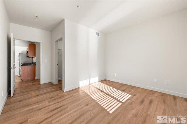 unfurnished bedroom featuring light wood-style floors, a closet, a spacious closet, visible vents, and baseboards