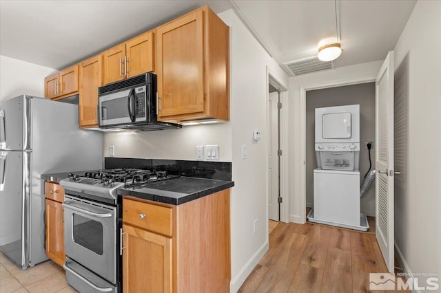 kitchen with light wood-style floors, visible vents, dark countertops, stainless steel appliances, and stacked washer and clothes dryer