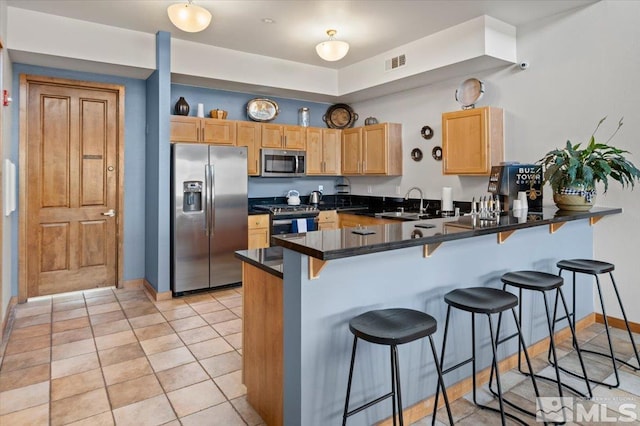 kitchen with visible vents, a sink, appliances with stainless steel finishes, dark countertops, and a peninsula