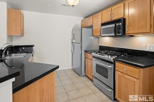 kitchen with appliances with stainless steel finishes, light tile patterned floors, a sink, and dark countertops