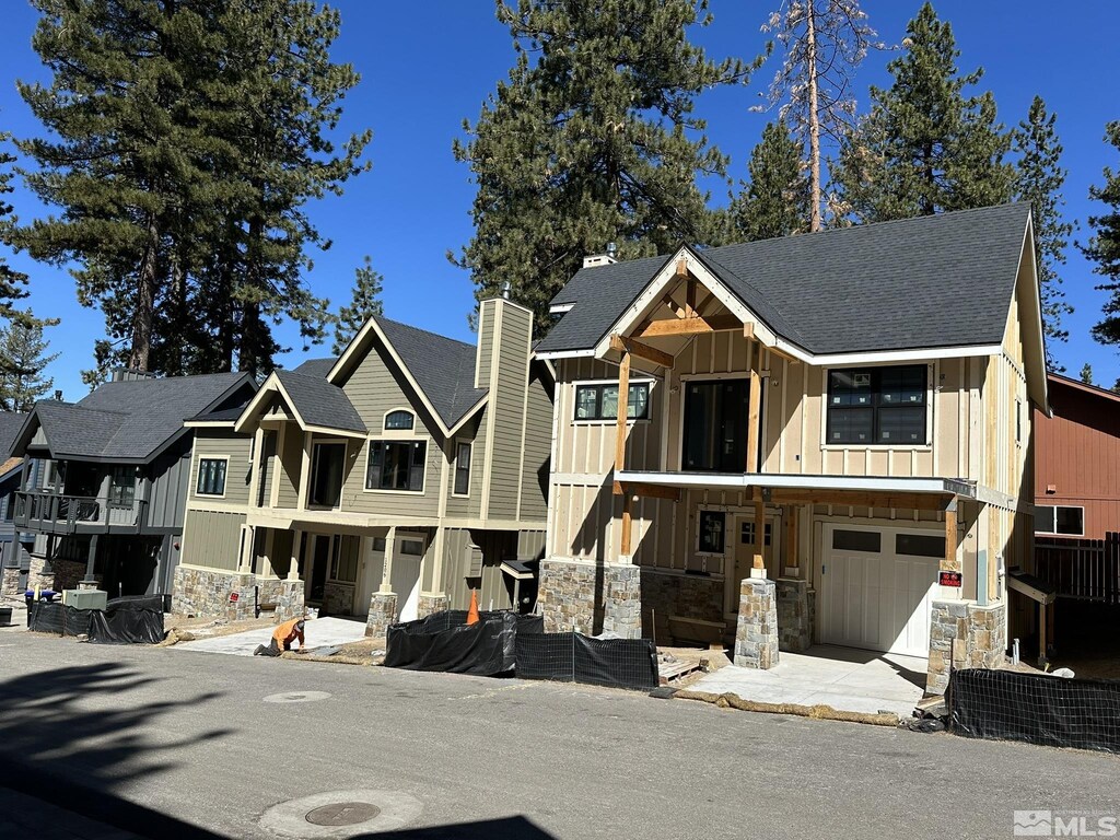 view of front of property featuring board and batten siding, stone siding, a chimney, a garage, and a residential view