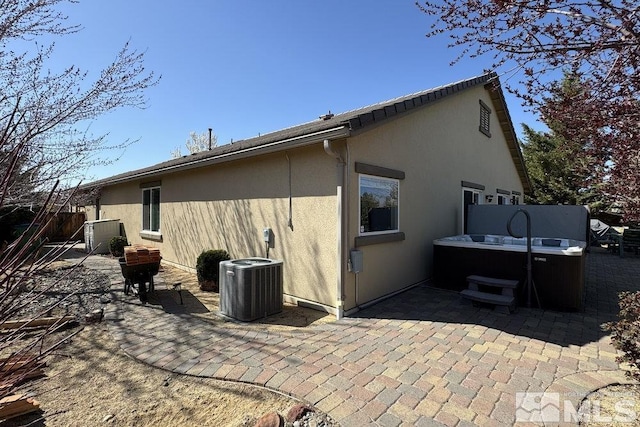 rear view of house with a patio, central air condition unit, stucco siding, a hot tub, and fence
