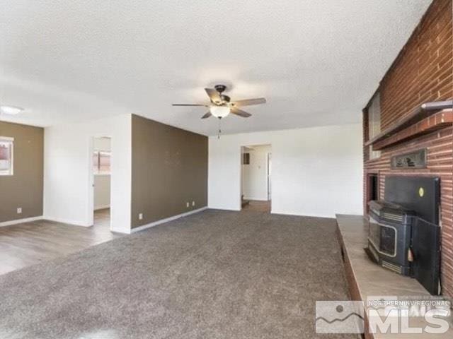unfurnished living room with a wood stove, a textured ceiling, a ceiling fan, carpet flooring, and baseboards