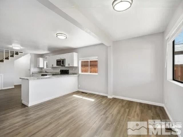 kitchen with dark wood finished floors, a peninsula, white cabinetry, stainless steel microwave, and light countertops