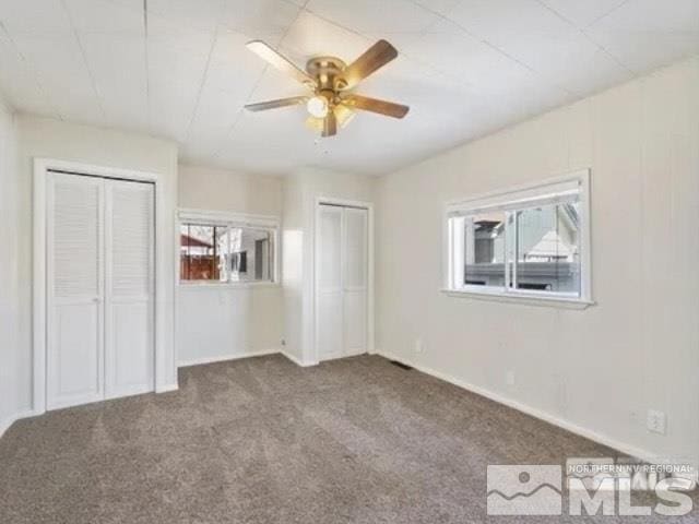 unfurnished bedroom featuring carpet, baseboards, two closets, and a ceiling fan