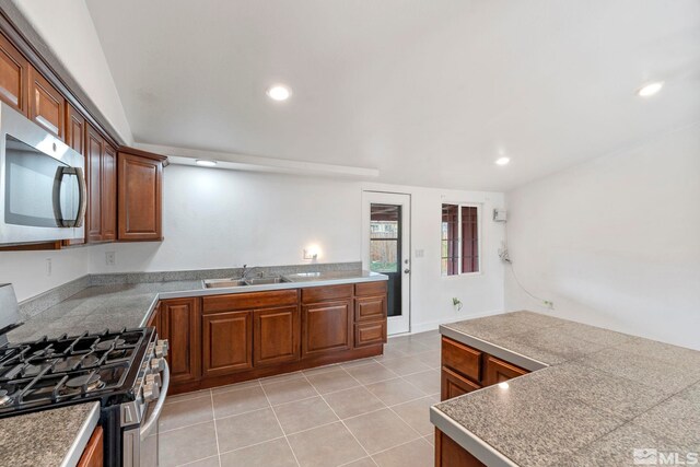 kitchen with brown cabinetry, light tile patterned floors, a sink, and stainless steel appliances