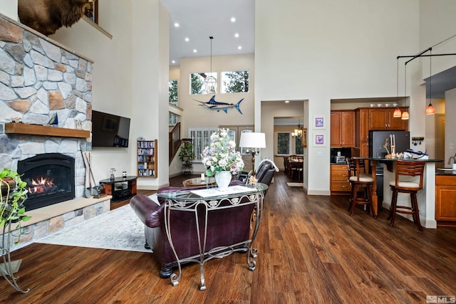living area with baseboards, dark wood-style floors, a fireplace, a towering ceiling, and stairs