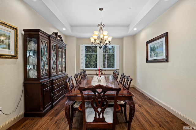 dining room featuring a chandelier, dark wood-type flooring, a raised ceiling, and baseboards