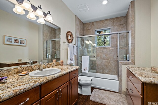 bathroom with vanity, visible vents, toilet, wood finished floors, and enclosed tub / shower combo