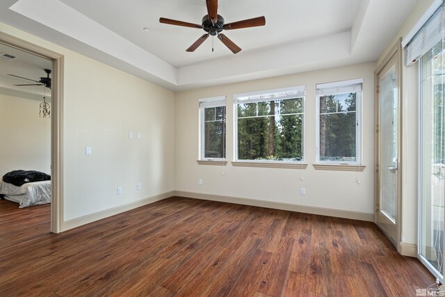 empty room featuring baseboards, visible vents, a tray ceiling, ceiling fan, and wood finished floors