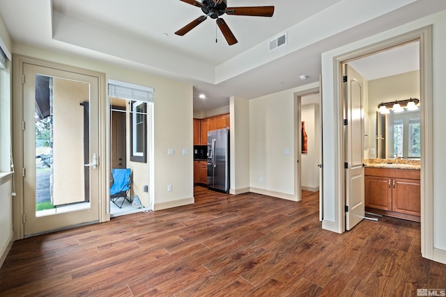 unfurnished living room featuring dark wood-style flooring, a ceiling fan, visible vents, a raised ceiling, and a sink