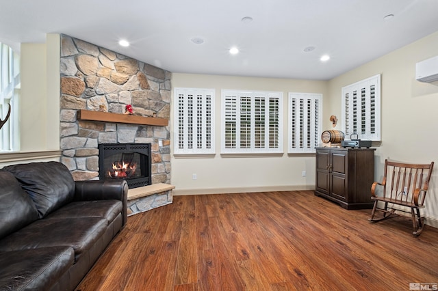 living room with baseboards, dark wood-style flooring, an AC wall unit, a stone fireplace, and recessed lighting