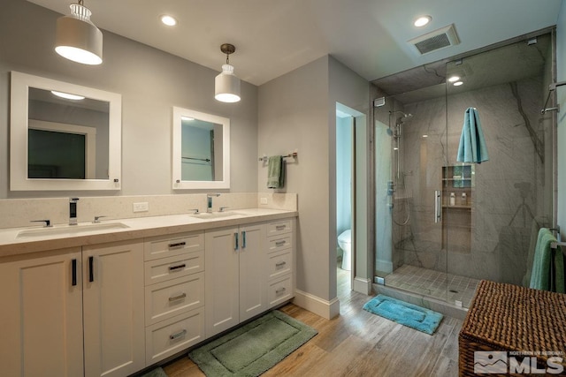 bathroom with a stall shower, wood finished floors, a sink, and visible vents