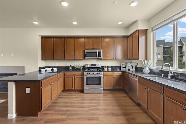 kitchen featuring a sink, appliances with stainless steel finishes, a peninsula, dark wood finished floors, and dark stone counters