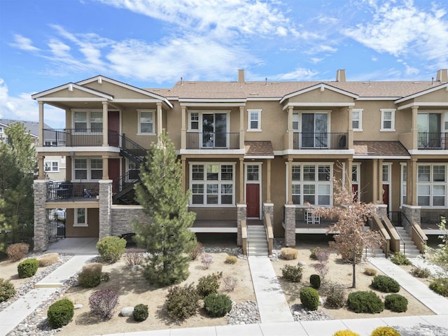townhome / multi-family property with roof with shingles, a chimney, and stucco siding