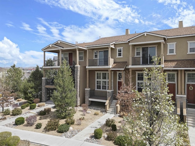 view of front facade featuring a balcony, stucco siding, a chimney, and a shingled roof