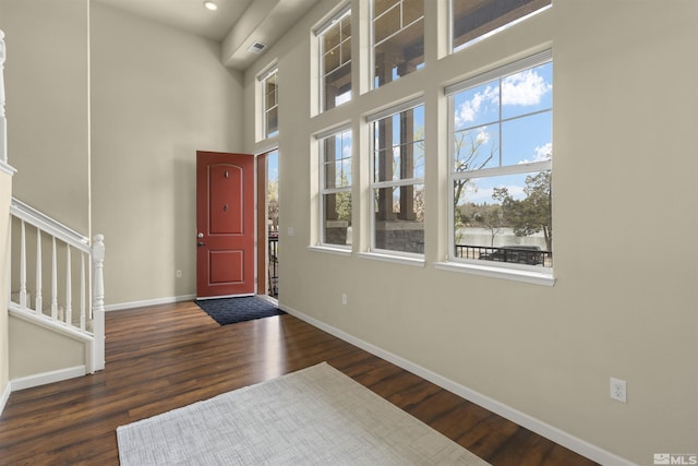 entrance foyer with dark wood-type flooring, baseboards, a towering ceiling, and stairs