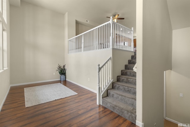 stairs featuring wood finished floors, ceiling fan, a towering ceiling, and baseboards