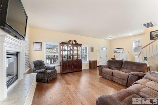 living room featuring a glass covered fireplace, baseboards, stairway, visible vents, and light wood finished floors