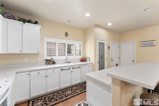 kitchen featuring white cabinets, white dishwasher, a kitchen breakfast bar, light wood-style floors, and range