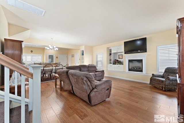 living room with a chandelier, a glass covered fireplace, visible vents, and hardwood / wood-style flooring