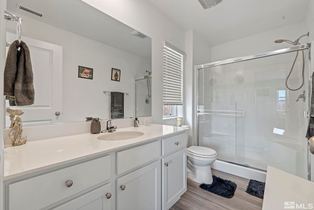 bathroom with toilet, wood finished floors, vanity, and a stall shower