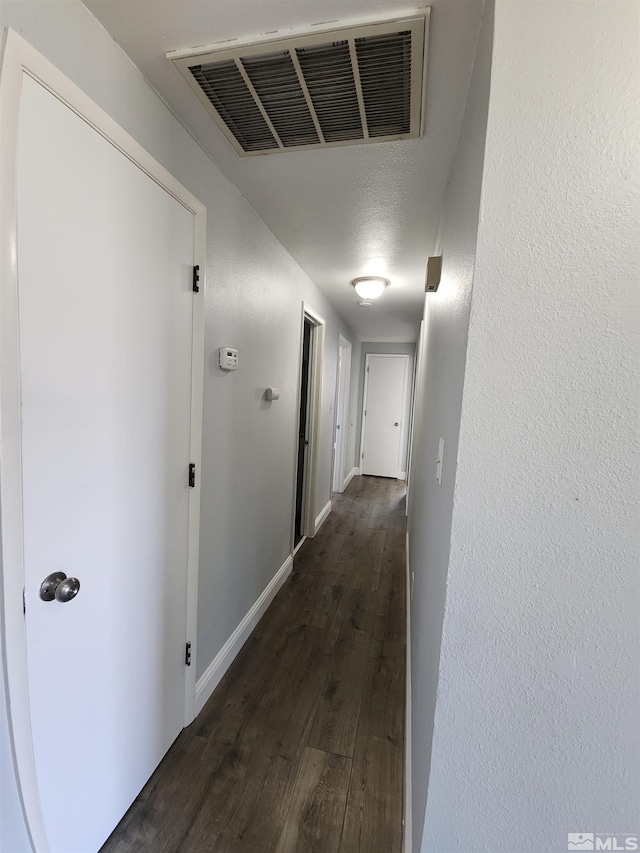 hall featuring visible vents, dark wood-style flooring, and baseboards