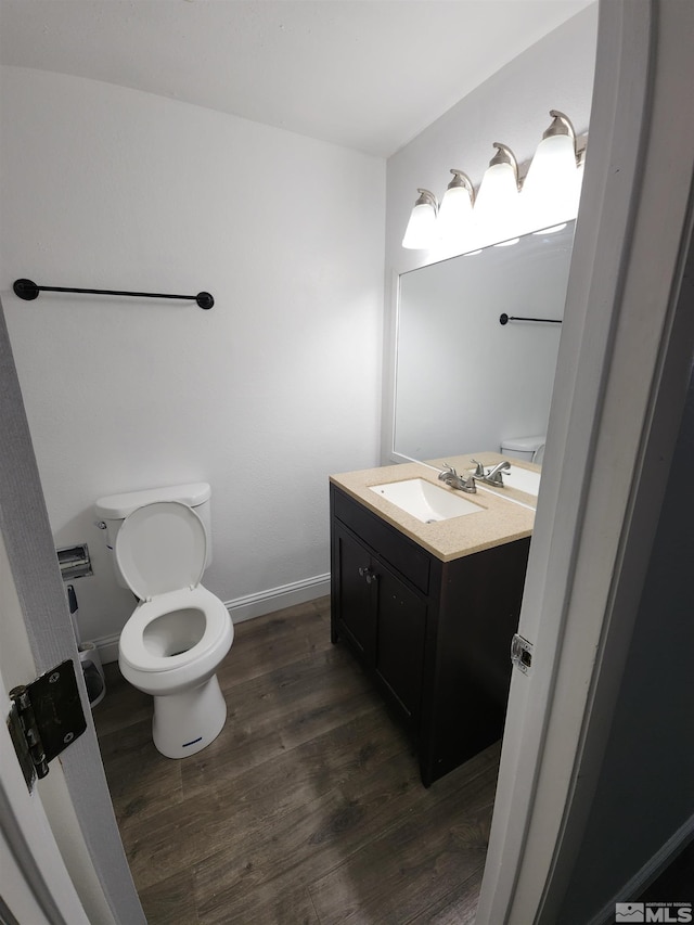 half bathroom with toilet, vanity, wood finished floors, and baseboards