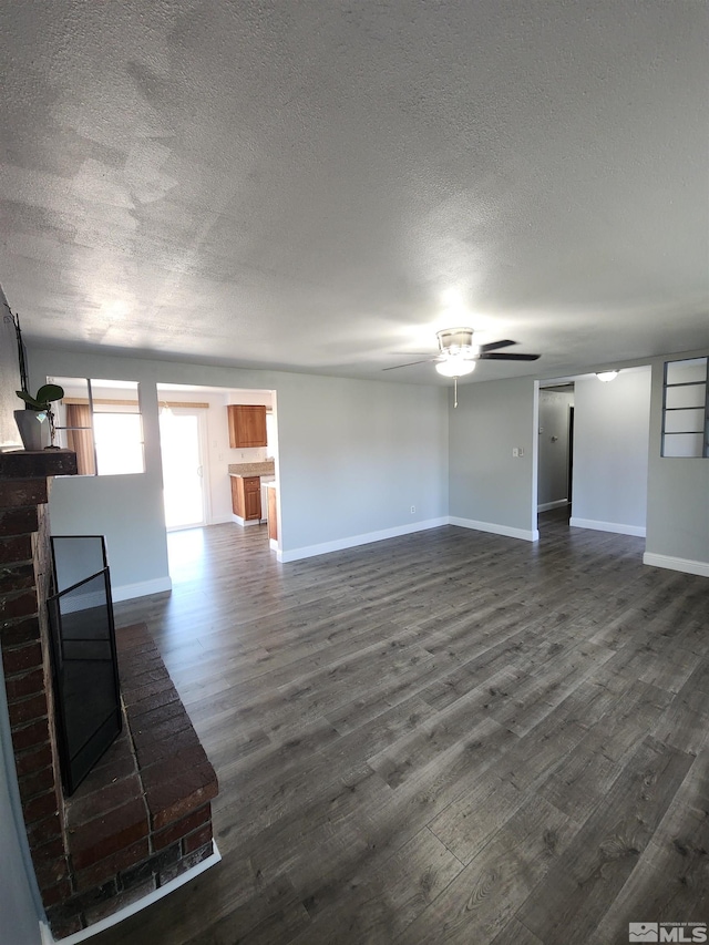 unfurnished living room featuring ceiling fan, dark wood-style floors, baseboards, and a textured ceiling