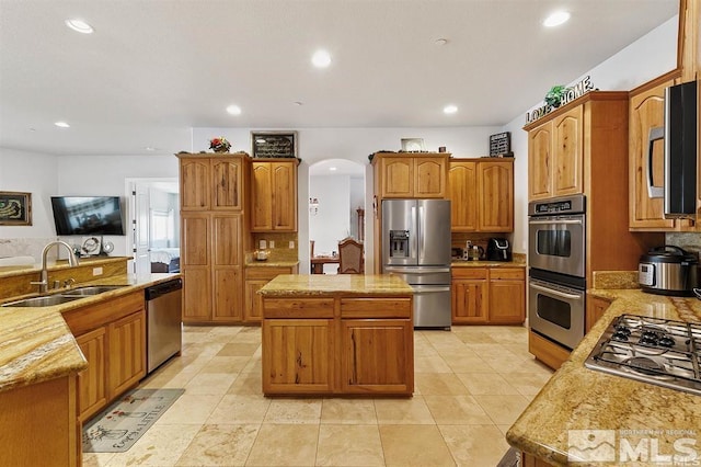 kitchen with arched walkways, a sink, light countertops, stainless steel appliances, and a kitchen island