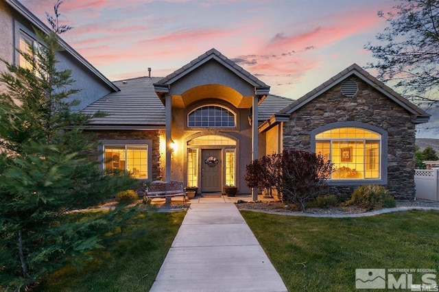 view of front of house with a tiled roof, stucco siding, stone siding, and a front lawn
