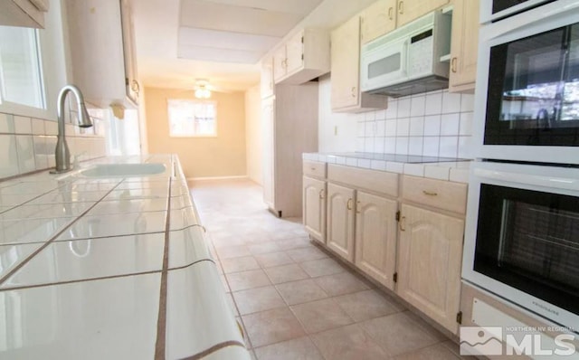 kitchen featuring baseboards, tile counters, white appliances, backsplash, and a sink