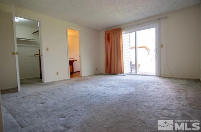 unfurnished bedroom featuring ensuite bathroom, a textured ceiling, a walk in closet, access to exterior, and carpet