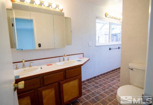 full bathroom featuring a sink, toilet, double vanity, and baseboards