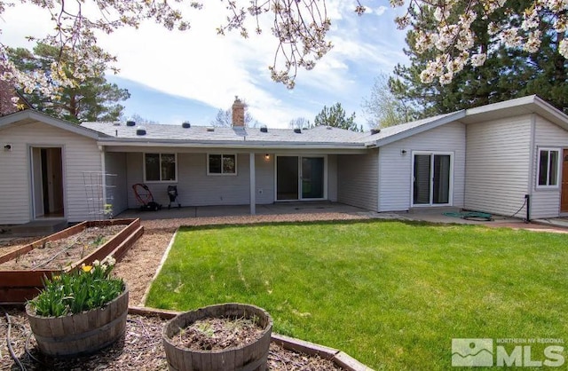 back of house with a yard, a patio area, a vegetable garden, and a chimney
