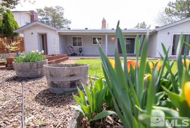 rear view of property with a chimney, fence, and a vegetable garden