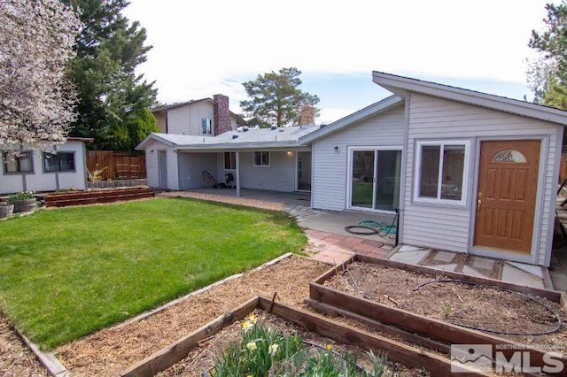 rear view of property featuring a yard, a garden, fence, and a patio