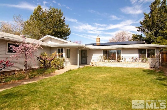 back of property with a yard, roof mounted solar panels, and a chimney