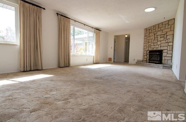 unfurnished living room featuring a stone fireplace, carpet flooring, and a textured ceiling