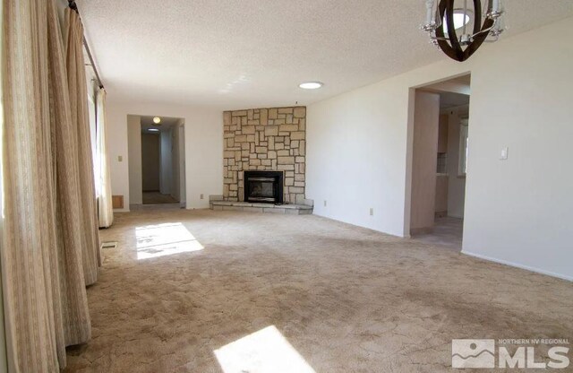 unfurnished living room featuring a stone fireplace, carpet flooring, a notable chandelier, and a textured ceiling