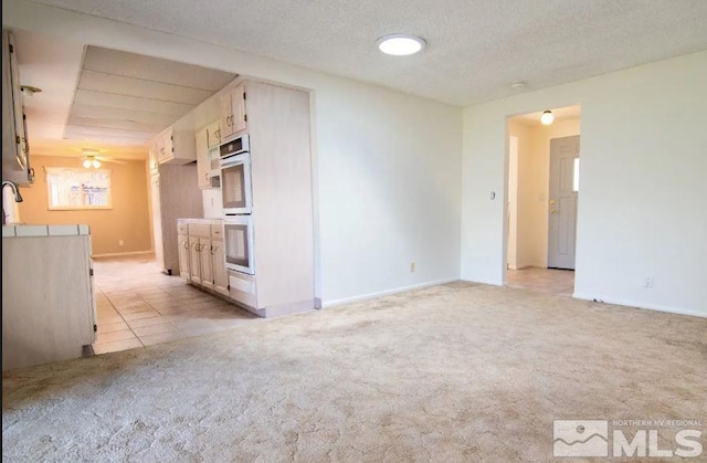unfurnished living room featuring a textured ceiling, light colored carpet, a sink, and light tile patterned floors