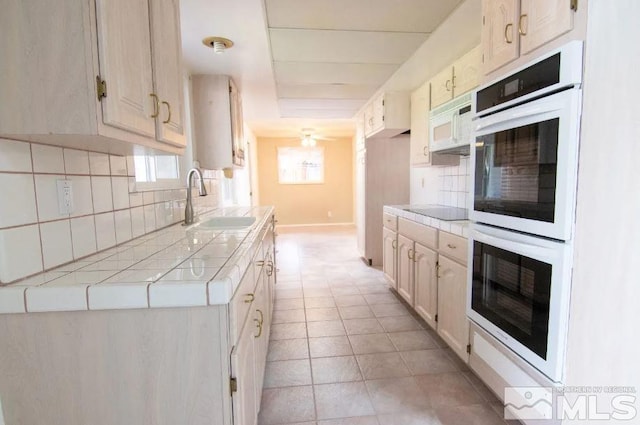 kitchen with tile counters, white appliances, a ceiling fan, decorative backsplash, and a sink