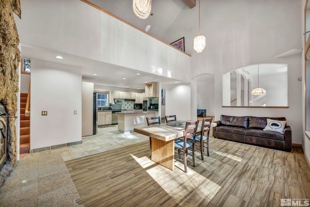 dining room with a towering ceiling, recessed lighting, stairs, arched walkways, and light wood finished floors