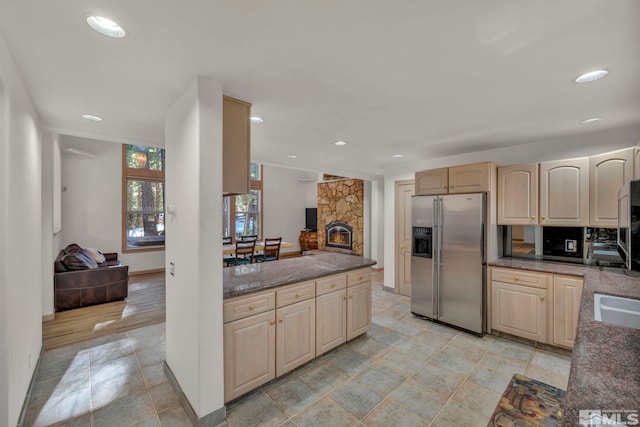 kitchen with baseboards, stainless steel fridge, light brown cabinets, a stone fireplace, and recessed lighting