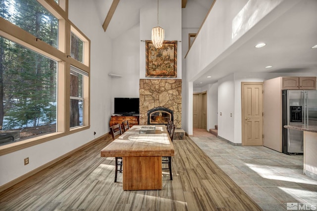 living area featuring a stone fireplace, baseboards, recessed lighting, light wood-style flooring, and high vaulted ceiling